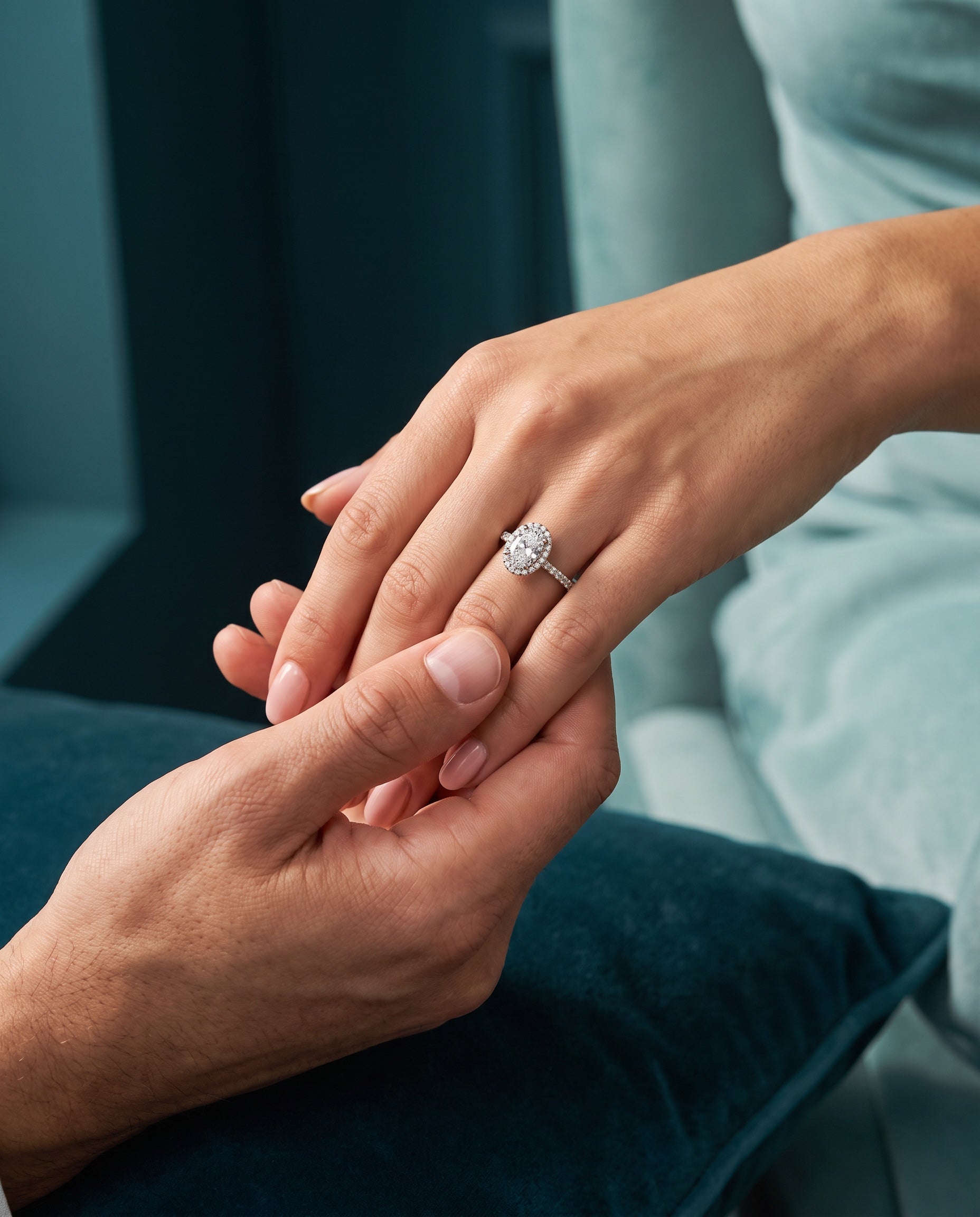An oval diamond halo ring on a hand held by a partner